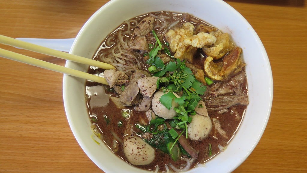 A bowl of Thai noodles with pork, meatballs, crackling, and cilantro